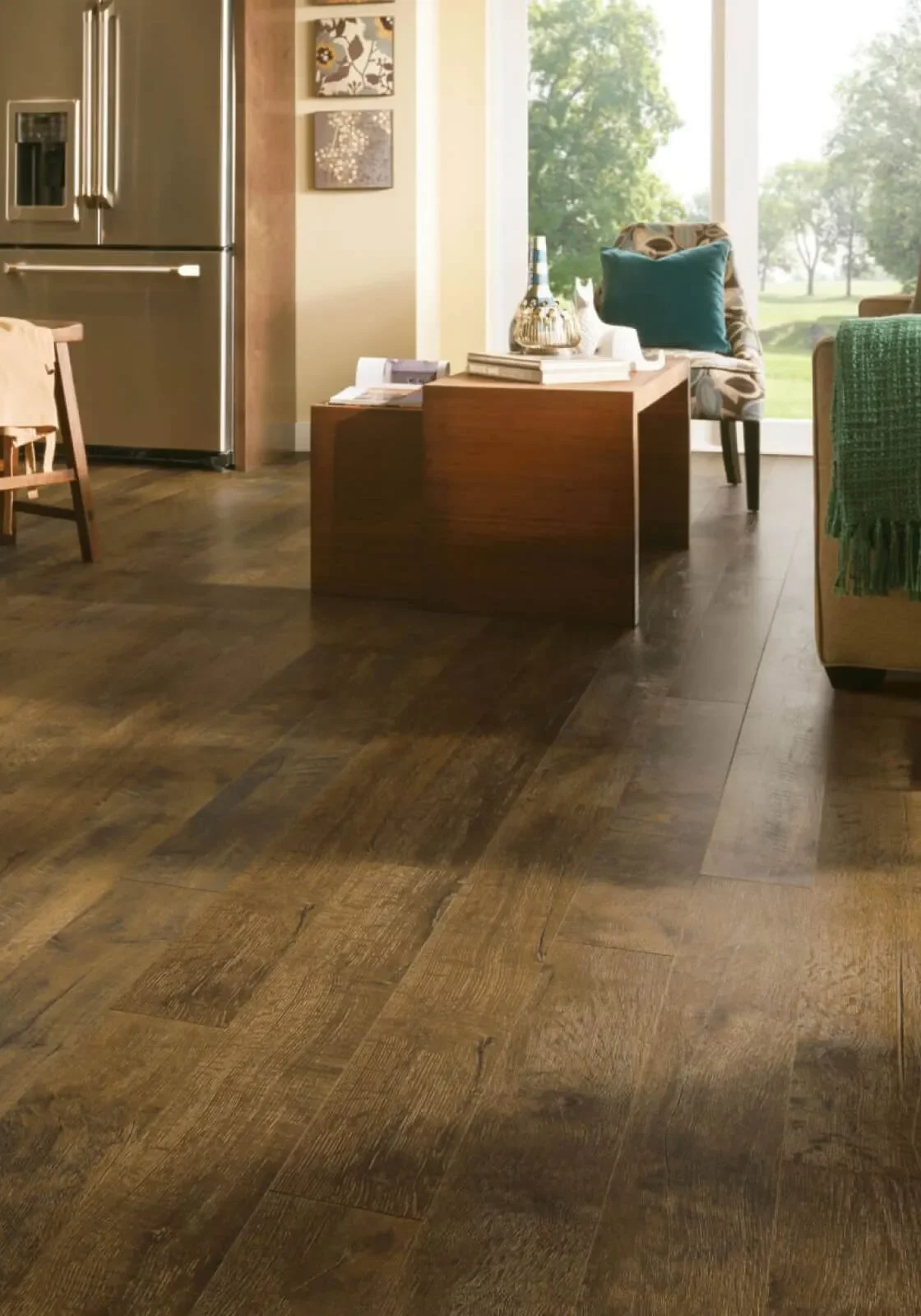 Dark brown wood-grain luxury vinyl plank flooring in a warm, inviting living room featuring a wooden coffee table and a large window looking out to trees.