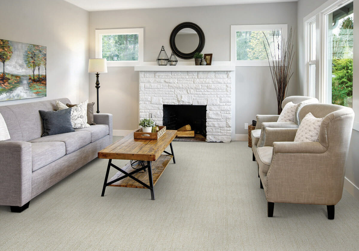A bright, modern living room featuring a white brick fireplace, neutral furniture, and light-colored patterned carpeting.