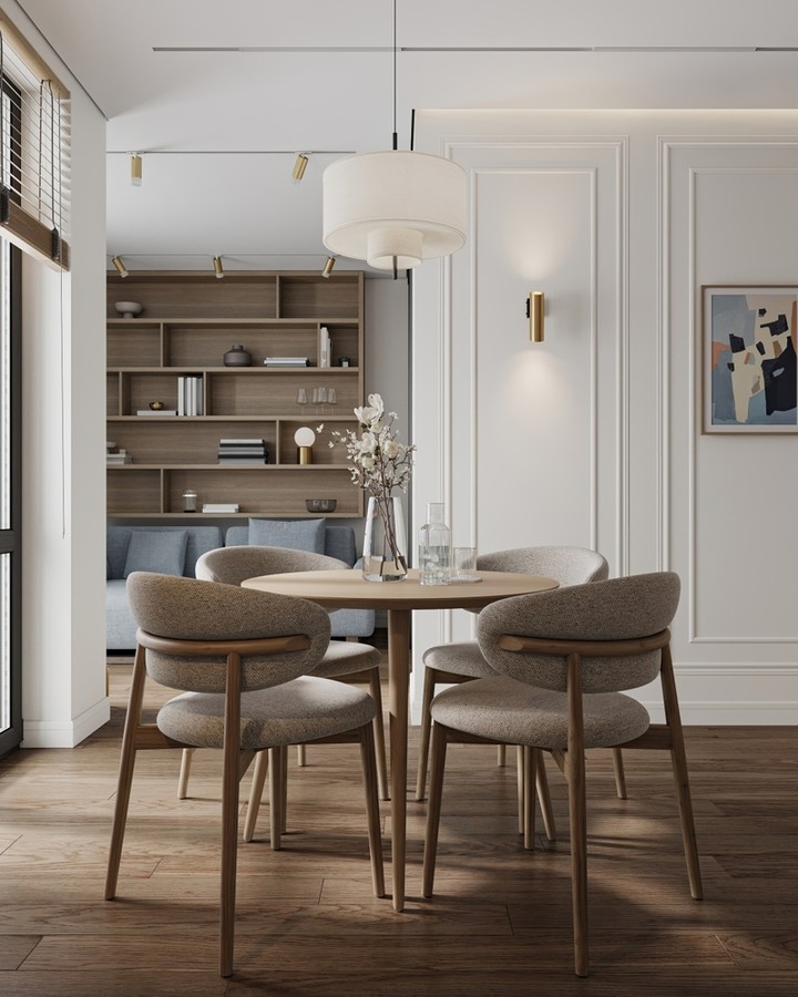 Close-up of a modern round wood dining table with upholstered chairs over dark wood plank flooring.