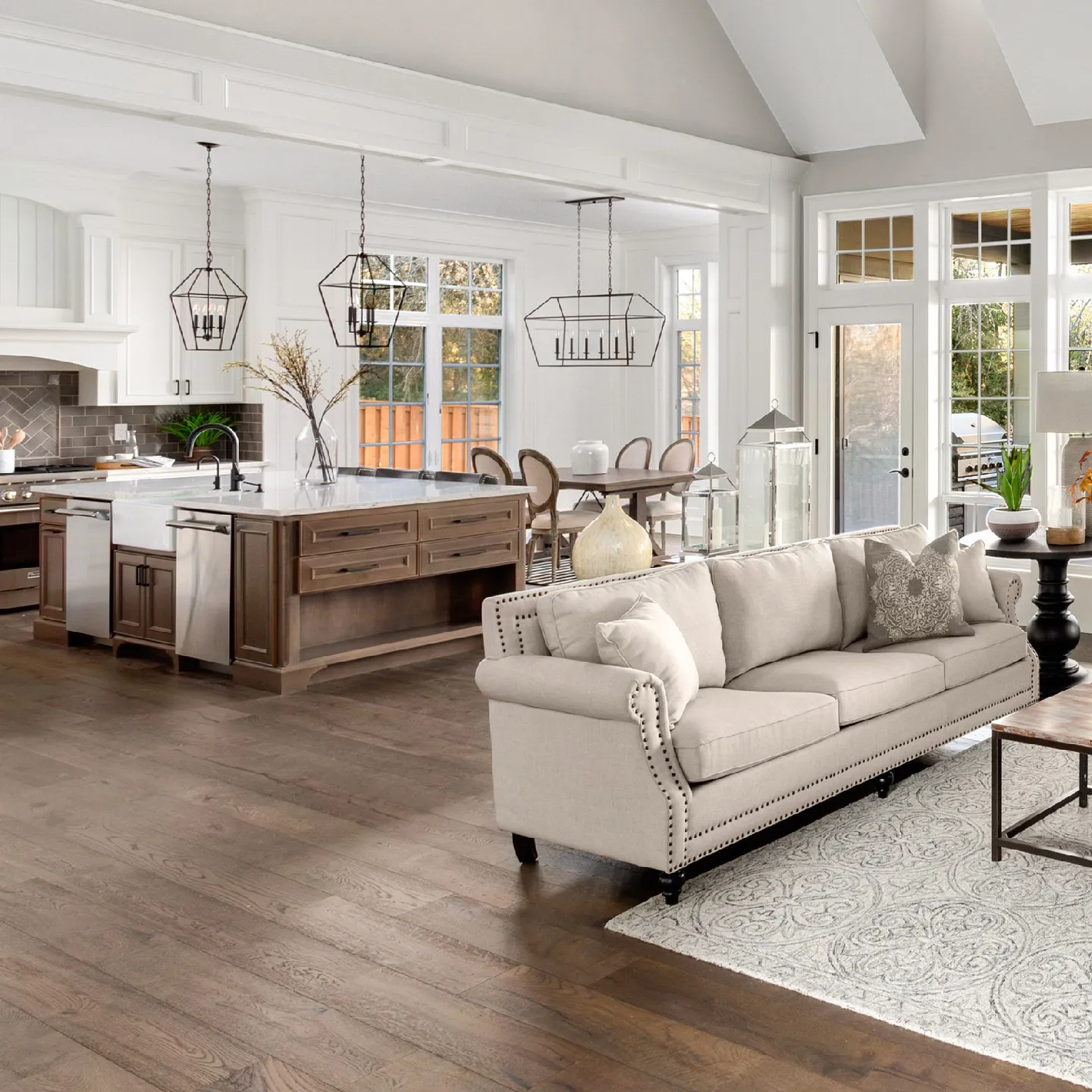 Wide view of a modern open-concept home interior with dark wood plank flooring, a light chesterfield sofa, and a kitchen island.