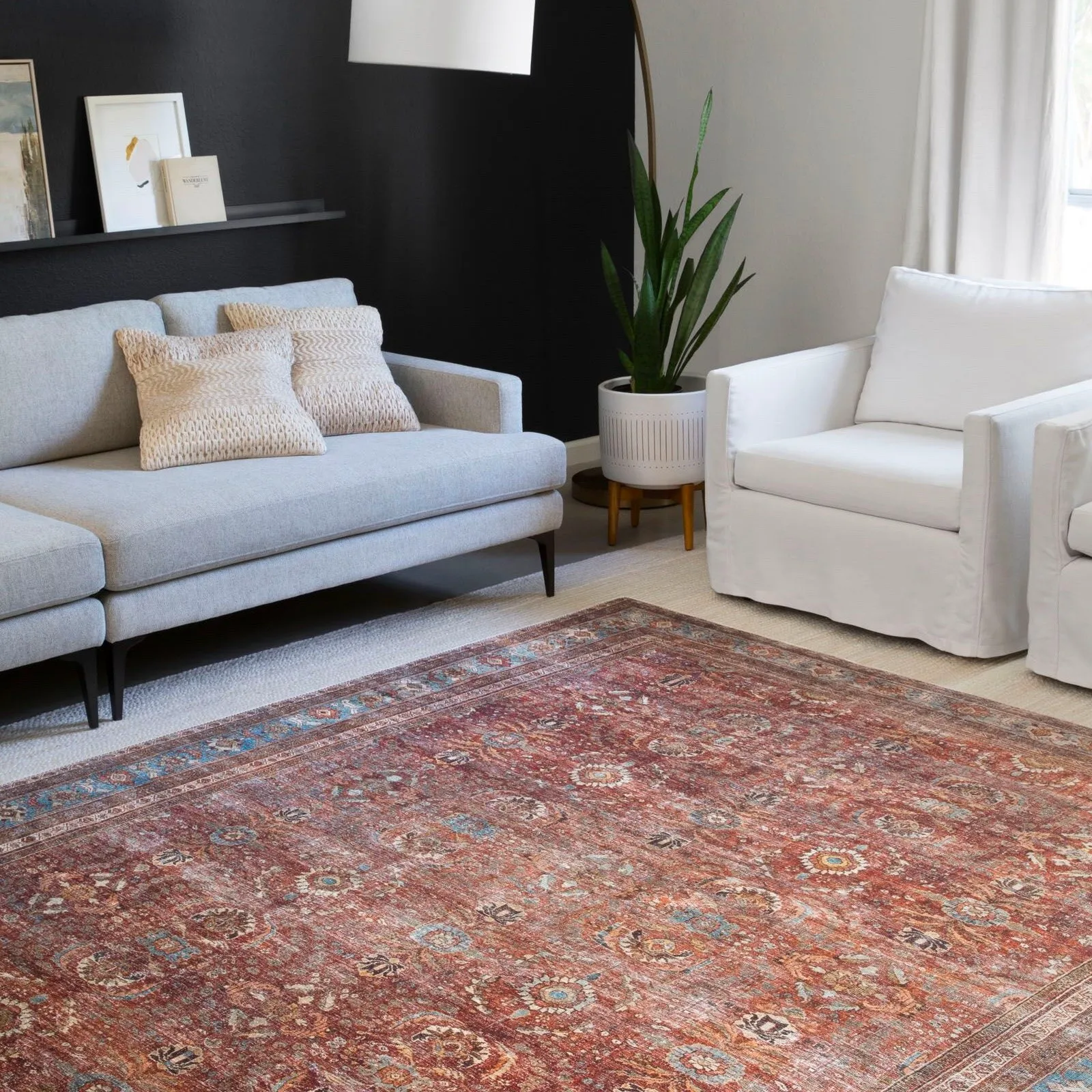 Terracotta-colored traditional area rug with intricate patterns centered in a modern living room with a grey sofa and black accent wall.