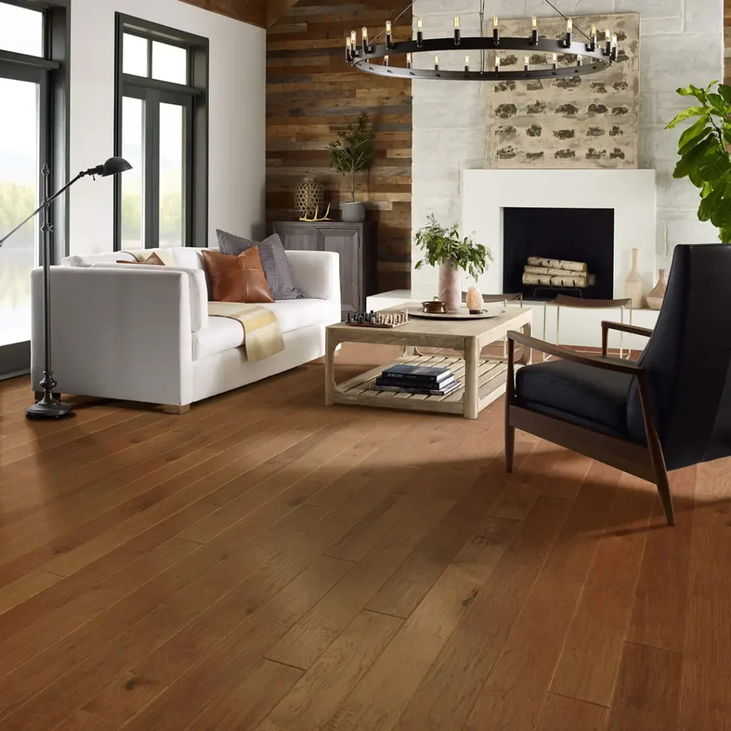Medium-brown plank hardwood flooring in a rustic-modern living room with a stone fireplace, white sofa, and a large round metal chandelier.