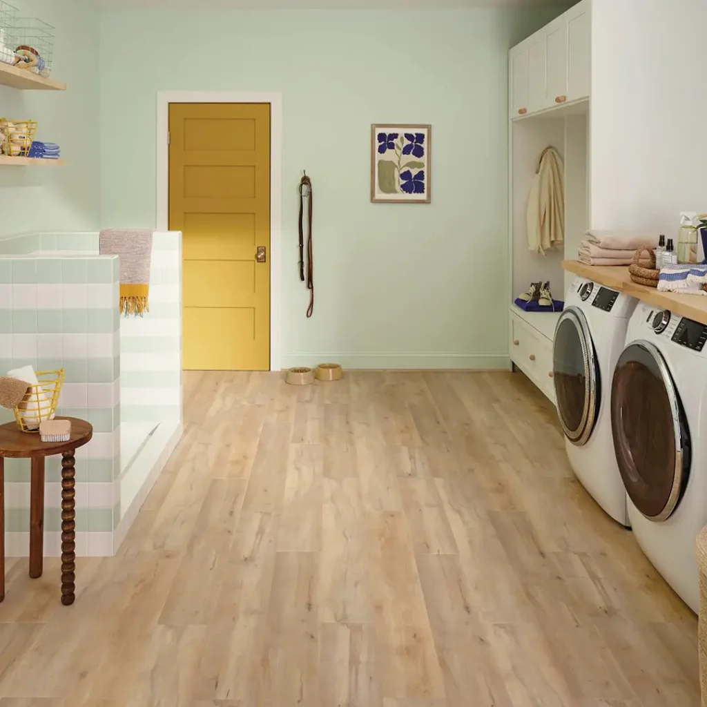 Light, natural wood-look vinyl plank flooring in a vibrant laundry and pet-care room with mint green walls and a bold yellow door.