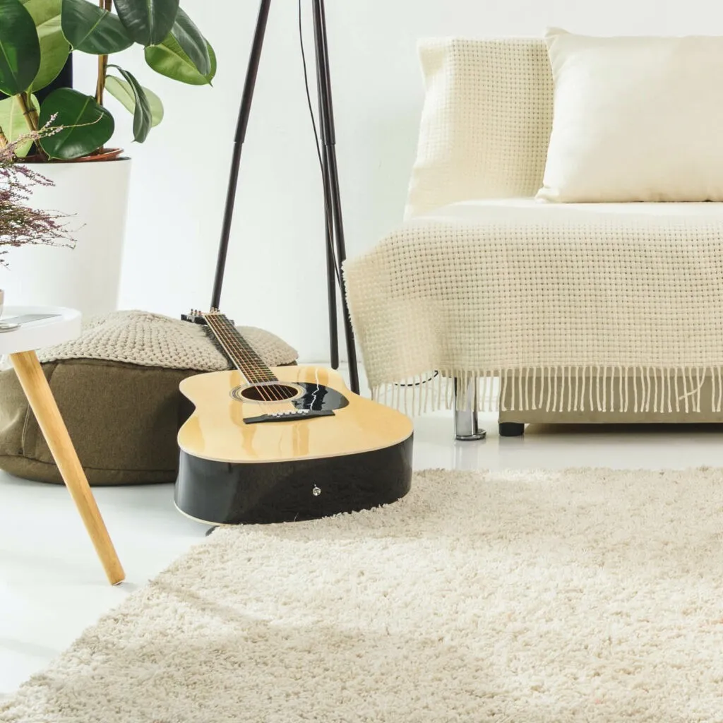 A cozy room setting showcasing a plush cream area rug, a fringed daybed, and an acoustic guitar resting on the floor.